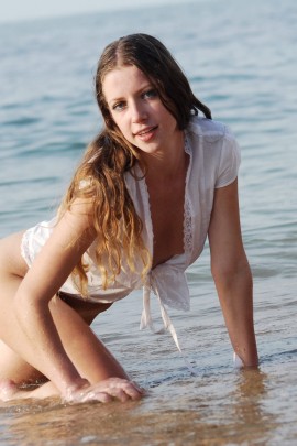 Голая девушка стоит раком на пляже в песке
